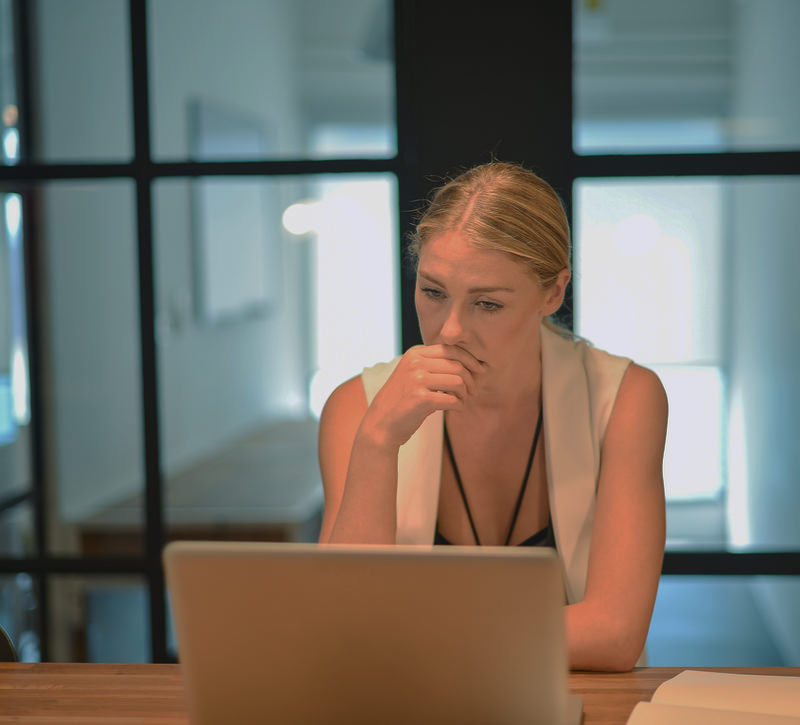 Vrouw achter laptop zittend kijkt heel serieus naar een website.