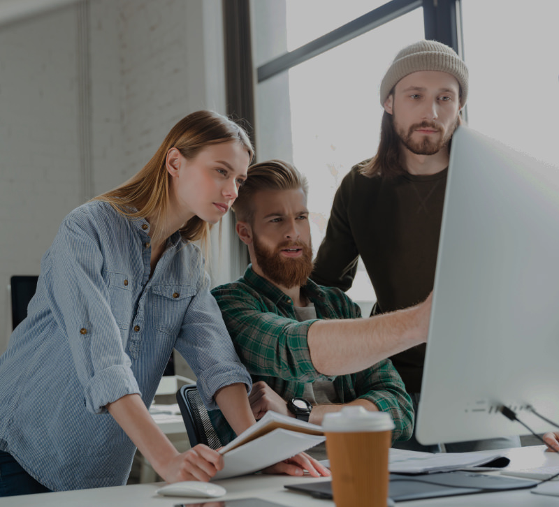 Een vrouwelijke en 2 manlijke webdesigners bekijken een website op een grote monitor in de studio van AllMediaLab webdesign.