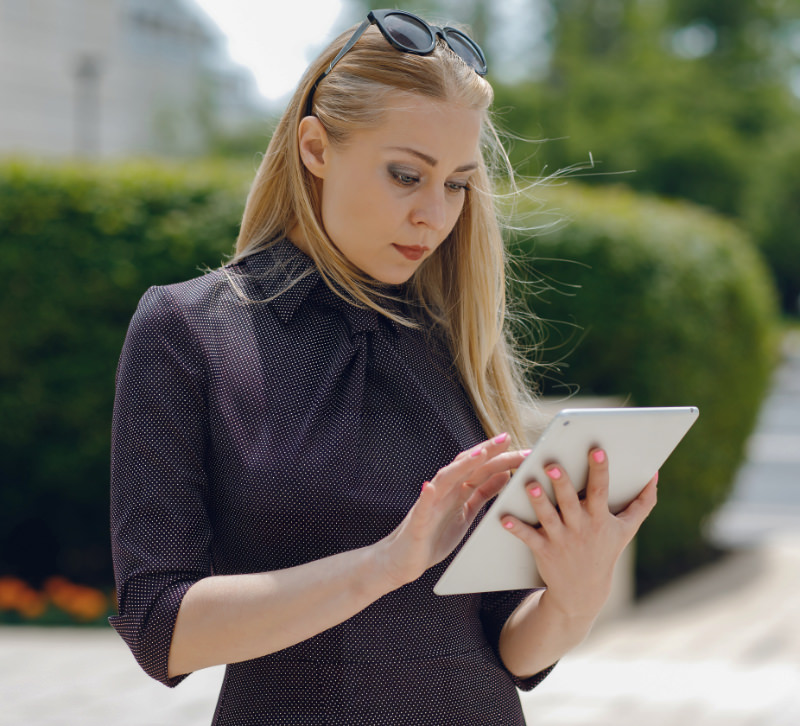 Blonde vrouw staat buiten op straat te kijken naar haar tablet met daarom haar nieuwe website.