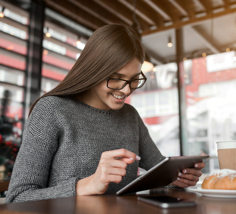 Vrouw zit in koffieshop op een tablet te kijken en zoekt een bedrijf in Google Search