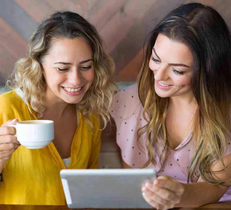 Two friends are laughing together, looking at a tablet with their new company website.