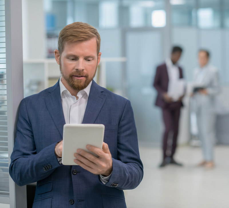 Een man met rood haar en een baardje kijkt in een kantoor op zijn tablet naar een website.