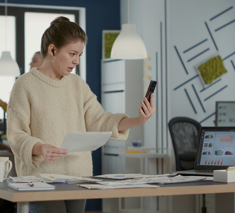 Vrouwelijke webdesigner kijkt naar haar telefoon in de AllMediaLab webdesign studio om een website te controleren.