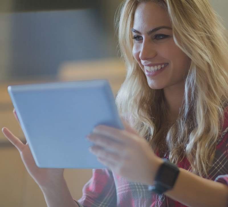 Woman smilingly looks at her tablet, which she holds in her hand to look up something in Google Search.