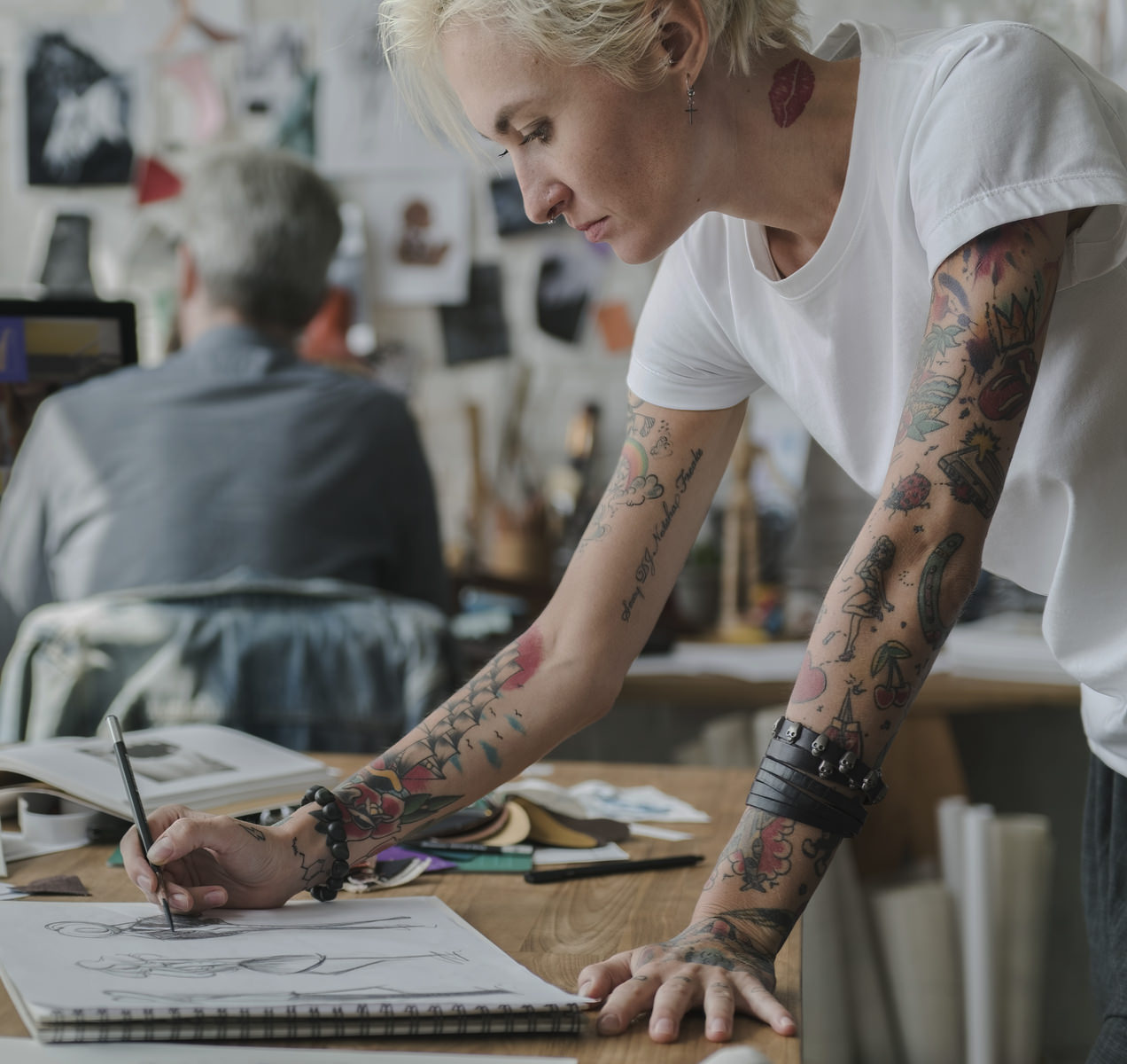 Een jonge vrouw in onze AllMediaLab webdesign studio met veel tattoos is bezig met een ontwerp door een schets te maken op papier.