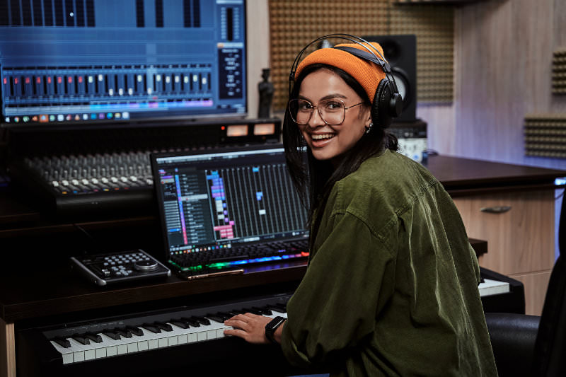 Vrouwelijke geluidstechnicus zit achter een mengpaneel een muziekstuk te mixen.
